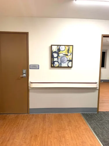 Entrance to a public restroom beside a wooden door, featuring a colorful abstract painting on the wall